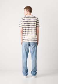 Tricou rayé în crem și marin, cu mâneci scurte, croială lejeră, asortat cu blugi de un albastru deschis și adidași albi, văzut din spate.