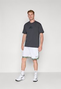 Grå T-shirt med et grafisk logo på brystet, parret med hvide shorts med et farverigt, mønstrede kant og Nike-branding, båret med sneakers.