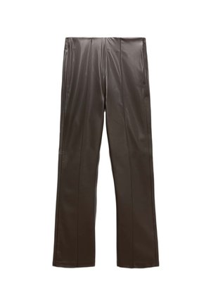 Donna che indossa pantaloni svasati in finta pelle marrone scuro e un maglione rosa chiaro, in piedi con ballerine nere.