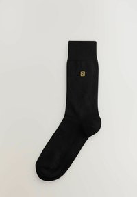 Sort bomuldsstrømpe med ribbet skaft, prydet med et lille gult broderet logo. Glat tekstur og ankel-længde design.