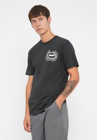 Black cotton t-shirt with a crew neck, featuring a white graphic design on the left chest area and short sleeves.