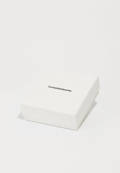 Λευκό κουτί από χαρτόνι με λεία υφή, ελαφρώς ανυψωμένο καπάκι, και μαύρο εκτυπωμένο κείμενο "Completedworks" στην κορυφή.
