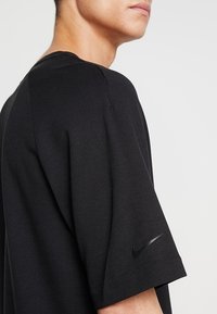 Svart Nike t-shirt med kortärmar, rundad halsringning och en subtil texturerad tyg. Inkluderar en liten svart logotyp på vänstra ärmen.