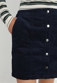 Marinblå kordkjol med vertikal ribsstruktur, prydd med fem silverfärgade tryckknappar fram och sidofickor.