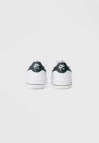 Nike Air tenisice s bijelim tijelom, crnim naglaskom na peti, teksturiranim panelom i potpisanom logotipom na leđima. Ravni bijeli potplat s detaljima zelenih pruga.