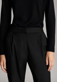 Schwarze, maßgeschneiderte Hosen mit Falten vorne, gefertigt aus glattem Stoff. Der Bund ist sauber gearbeitet, und sie haben ein gerades Bein.