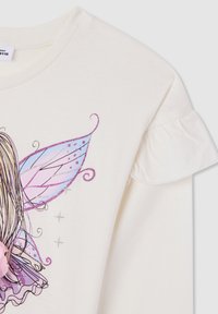 Camisetta a maniche lunghe color crema con dettagli arricciati sulle spalle e una grafica di una fata colorata con ali luccicose e un fiore di stoffa rosa.