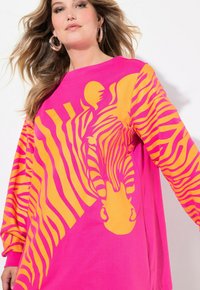 Felpa oversize rosa con strisce arancioni a zebra, caratterizzata da un design grafico centrale. Materiale in cotone morbido con maniche lunghe.