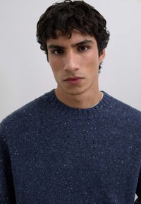 Suéter de punto azul marino con cuello redondo, textura moteada y puños acanalados. Diseñado con una silueta ajustada y tejido suave.