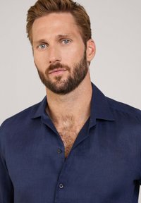 Camisa de lino azul marino con un cuello clásico, botonera delantera y pequeños botones marrones. Textura suave con un ligero brillo.