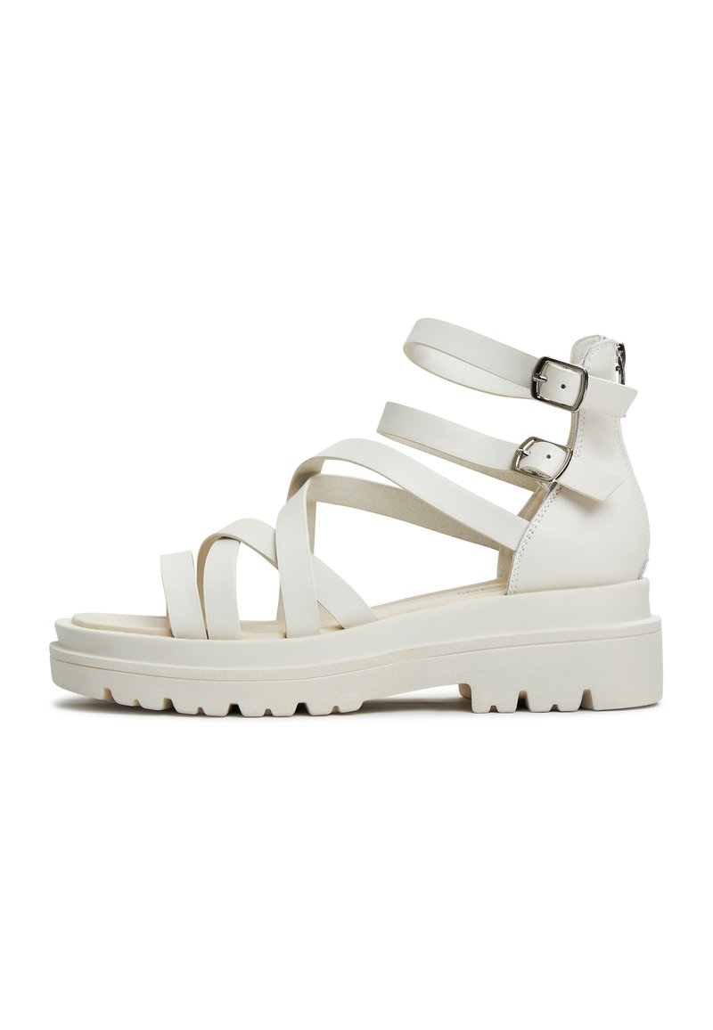 White strappy sandals with a chunky sole, featuring wide straps and adjustable buckles. Made from smooth synthetic material with a textured bottom.