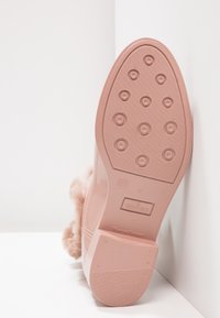 Suela de una bota de lluvia rosa con patrones de tracción circulares y un borde de piel sintética, inclinada contra una esquina de pared y suelo blancos.