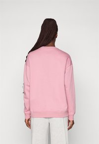 Felpa rosa con scollatura rotonda, maniche lunghe e orlo a coste. Tessuto morbido con un fit rilassato, abbinata a pantaloni grigi con coulisse.