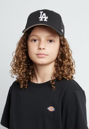 Cappellino da baseball nero con logo "LA" bianco, abbinato a una maglietta nera con un piccolo logo Dickies multicolore. Capelli ricci visibili.