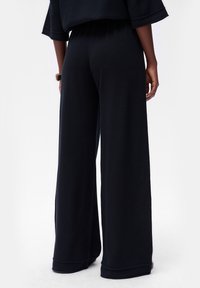 Zwarte, wijde broek met een gestructureerde afwerking en een elastische tailleband, met een comfortabele pasvorm die langs de enkel valt.