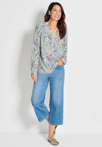Blusa leggera a fantasia floreale in colori pastello, abbinata a jeans a gamba larga blu chiaro e sandali verdi. Presenta un colletto con bottoni.