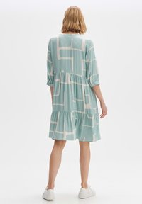 Helles blaues Kleid mit weißen geometrischen Mustern, drei Viertel-Ärmel, gestuftem Saum, aus weichem Stoff. Getragen mit weißen Turnschuhen.