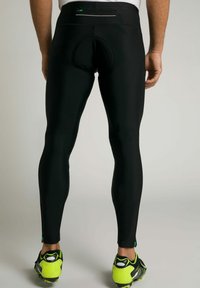 Schwarze sportliche Leggings mit schmaler Passform, ausgestattet mit einer Gesäßtasche und einer glatten, dehnbaren Textur. Neon-gelbe Laufschuhe sind sichtbar.