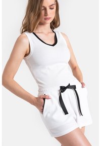 Biały dzianinowy top na ramiączkach z czarnym wykończeniem w serek, zestawiony z białymi szortami z elastycznym paskiem w talii i czarnym akcentem w postaci wstążki.