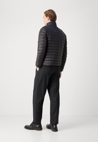 Giacca a vento nera con motivo trapuntato orizzontale, colletto alto e logo discreto, abbinata a pantaloni e scarpe neri.
