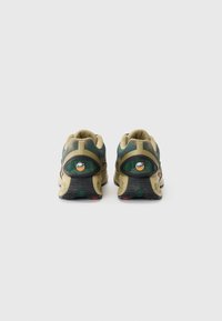Green and beige sneakers with a textured mesh upper, distinctive heel support, and black rubber outsole featuring colorful accent details.