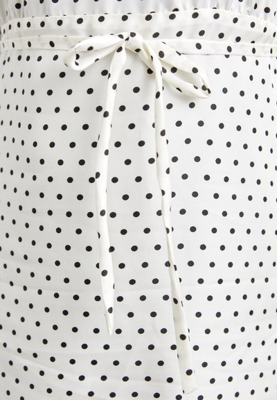 Weißer Stoff mit schwarzen Polka-Dots, der mit einem gebundenen Taillendetail und einer glatten Textur versehen ist. Das Design umfasst gleichmäßig verteilte, kreisförmige Muster.