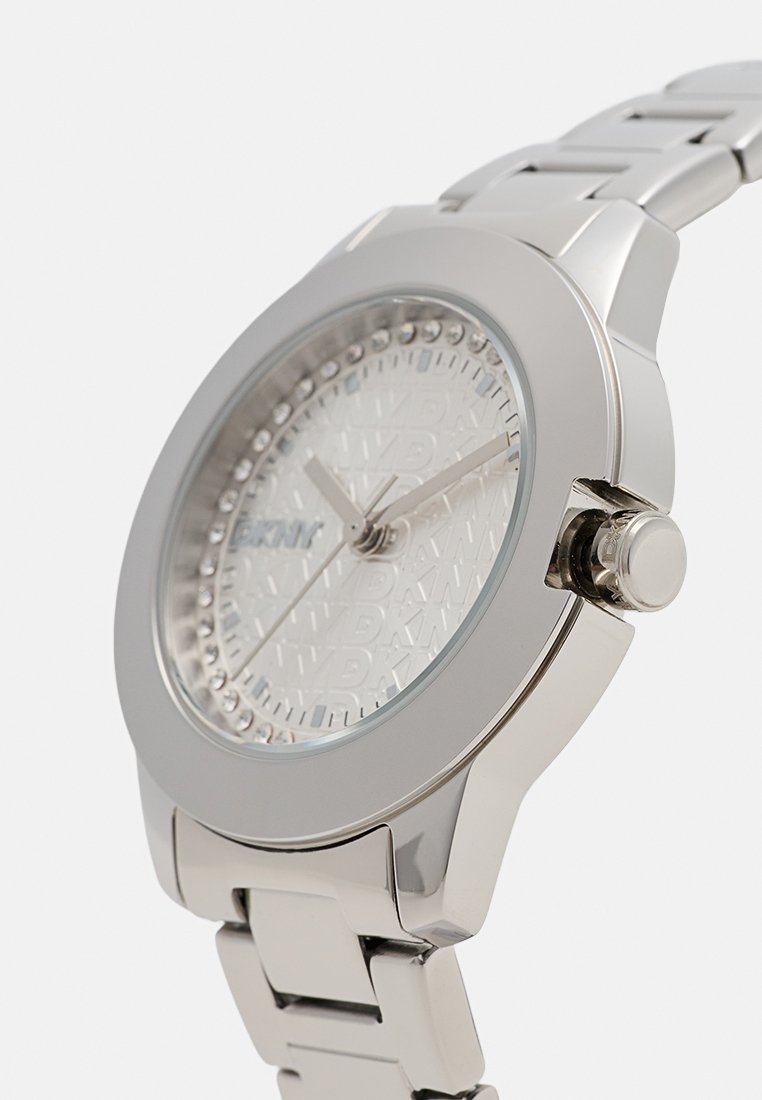 Reloj de acero inoxidable plateado con esfera de color gris claro texturizada, detalles similares a diamantes y acabado pulido en la correa y la caja.