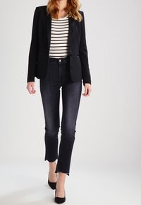 Černý blazer, pruhovaná košile a tmavé džíny; upravený design, přiléhavý střih, hladká textura a délka po kotníky s lemem s třásněmi.