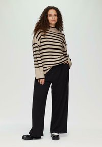 Beige en zwart gestreepte oversized trui met een hoge nek, gecombineerd met zwarte wijde broek met subtiele textuur en aangesloten mouwen.