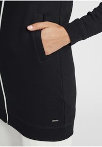 Crna pamučna majica s prednjim zatvaračem na patent, s bočnim džepovima, rebrastim manžetama i malim srebrnim logotipom na rubu.