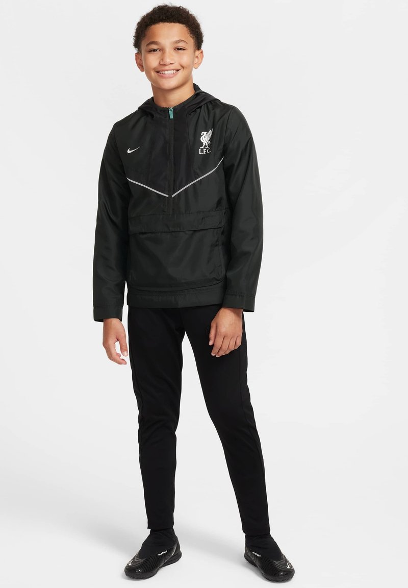 Czarna kurtka Nike z kapturem, z logo Liverpool FC i szarymi akcentami; noszona na czarnych spodniach i czarnych butach.