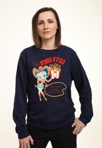 Námořnický modrý svetr s potiskem karikatury ženy v cowboyském klobouku, červenými akcenty a texty: "Betty's Wings O' Fire" a "Hot & Spicy."