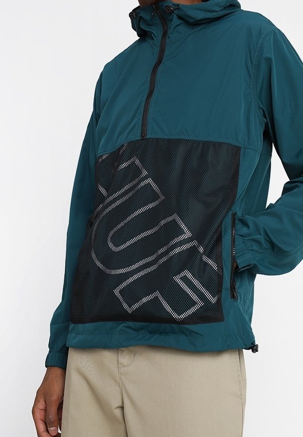 Tyrkysová lehká bunda s černou síťovinovou panelem, obsahující velké bílé písmo, nastavitelnou kapuci a boční kapsy, kontrastní textury látek.