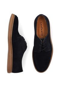 Czarne zamszowe buty z okrągłym noskiem, sznurowanym designem, kontrastującą brązową gumową podeszwą oraz teksturowaną wkładką z nazwą marki wewnątrz.