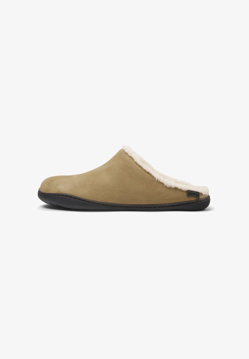 Tan suede slipper with a fluffy white fur lining and black rubber sole. Features minimal stitching and a logo on the side.