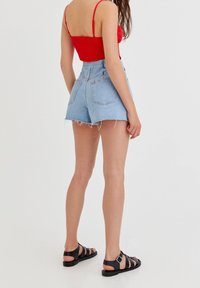 Denim shorts in light blue with frayed hem, paired with a red fitted top and black strappy sandals. Back view of model.