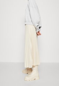 Sudadera de gran tamaño gris claro, falda midi crema con plisados y botas de combate beige con suela gruesa y cordones. Diseño minimalista y moderno.