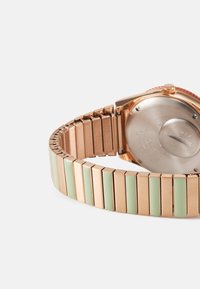 Montre en rose gold métallique avec un bracelet à motif. Présente des segments alternés de vert menthe solide et de rose gold poli. Fond de boîtier rond.