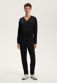 Set lounge nero con scollatura a V, maniche lunghe e pantaloni con vita elastica. Tessuto morbido con vestibilità rilassata e design minimalista.