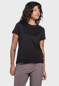 Schwarzes Baumwoll-T-Shirt mit lockerer Passform, kurzen Ärmeln, Rundhalsausschnitt und glatter Textur, kombiniert mit hellgrauen Hosen.