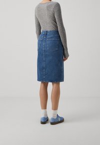 Džínová sukně s rovný střihem, modrým praním a zadními kapsami. Kombinována se šedým vroubkovaným topem a modrými teniskami s bílými akcenty.