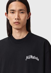 Sort bomulds-T-shirt med rund halsudskæring, med hvidt broderet tekst "AllSaints London" på venstre brystområde.