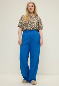 Losse beige en bruine luipaardprint top, gedragen met felblauwe, hoge taille broek met een knoopsluiting. Zachte schoenen.