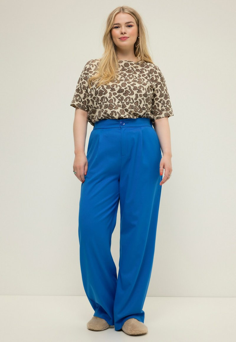 Losse beige en bruine luipaardprint top, gedragen met felblauwe, hoge taille broek met een knoopsluiting. Zachte schoenen.