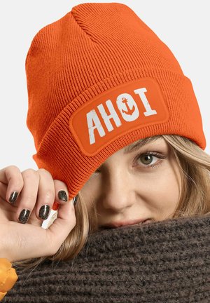 Orange knitted beanie with a rectangular patch featuring "AHOI" and an anchor graphic. Close-up showing texture and branding details.