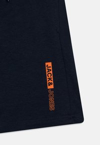 Mörkblått tygstycke med den orange "JACK & JONES" logotypen tryckt vertikalt nära den sydda sömmen och fållen.