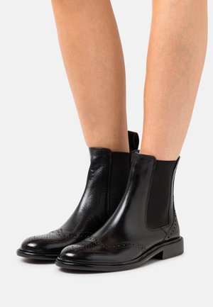 Bottines en cuir noir avec une finition lisse, panneaux latéraux élastiques, détails en brogue sur les bouts et un petit talon carré.