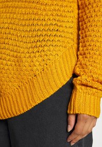 Maglione a maglia di un giallo vivace con un motivo testurizzato, polsini e orlo a costine. Il materiale sembra morbido, con una vestibilità comoda.
