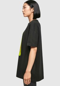 Black oversized T-shirt made of cotton, featuring a bright green graphic on the front. Short sleeves, round neckline, relaxed fit.
