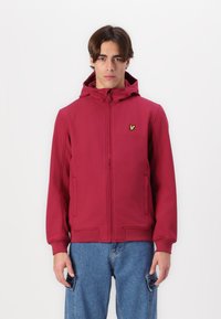 Sweatshirt vermelho com fecho zip, com um acabamento texturizado, apresentando capuz e bolsos laterais, e um pequeno logótipo verde no peito. Combinado com jeans azul claro.